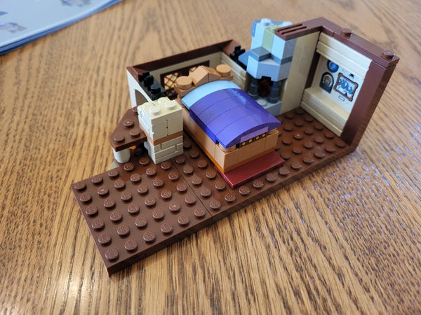 Bag 3 of the Lego Dungeons & Dragons set. This section depicts a partial build of the second floor of the inn, presumably a living space. There's a sticker on one wall depicting images that may be significant. There's a tiny fireplace in one corner, corresponding to the one downstairs. There's also a large bed with blue and purple blankets.