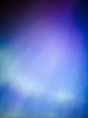 Flare-like aurora, with purples on top, neon whites and blues on bottom, some stars shining through 