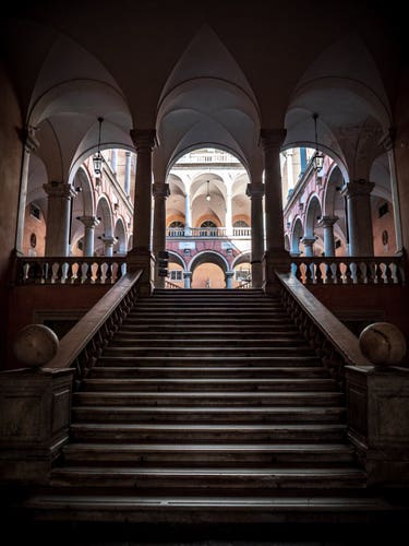 A big stairway leads up to a light filled foyer inside an old building in Italy