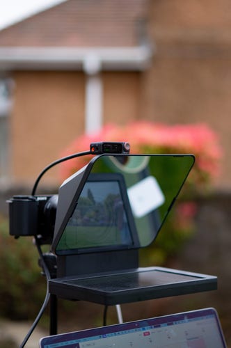 Elgato Prompter set up in a garden, with laptop below, hanging off a Sony mirrorless camera.