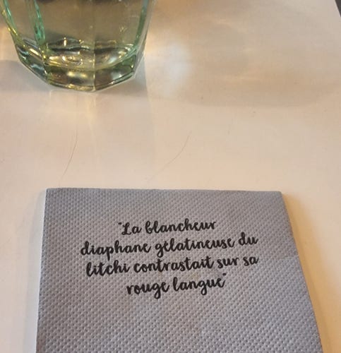 Photographie d'une serviette de restaurant. Il est écrit en font pseudo-caligraphiée "La blancheur diaphane gélatineuse du litchi constrastait sur sa rouge langue"