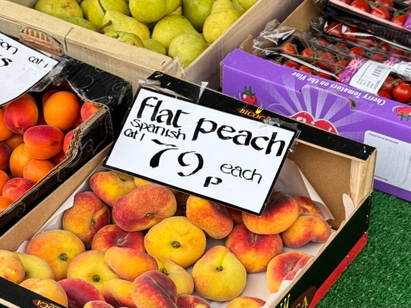 handwritten sign on a box of peaches outside a greengrocers: “flat peach (Spanish), Cat 1, 79p each”