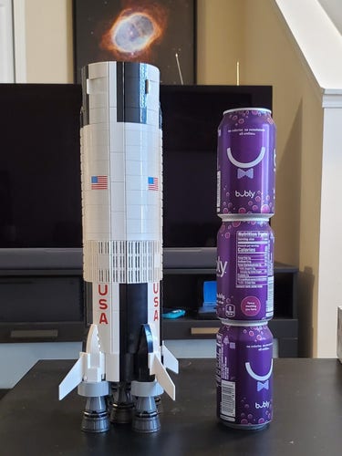 Completed first stage of the Saturn V Lego set next to a stack of soda cans. The first stage is about 3.5 cans tall and 1.5 times as wide.