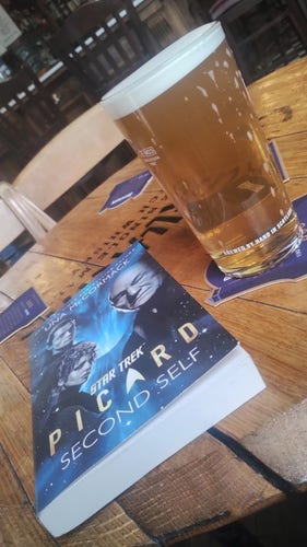 Copy of Picard: Second Self by Una McCormack next to a pint of ale on a pub table made from the top of an old whisky barrel