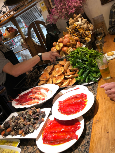 Pintxo bar with displayed food. Mushrooms, peppers, prawns, marinated red peppers, glasses of beer all on bar top.