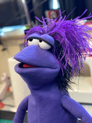 A purple Fraggle-like professional puppet made from polar fleece looking off into the distance
