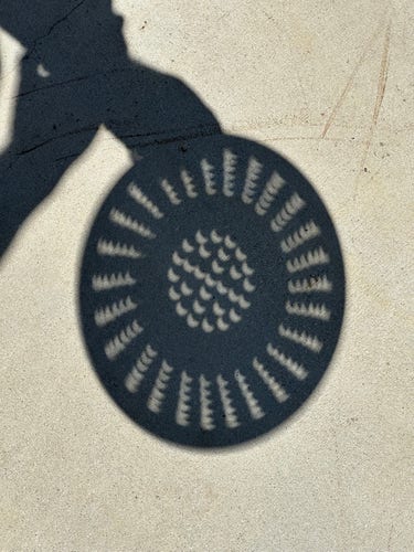 Shadow of a metal colander, projecting dozens of images of the partial eclipse in circular patterns
