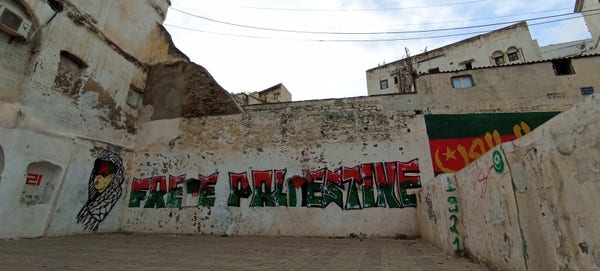 Graffiti Free Palestine au couleurs du drapeau palestinien, qui occupe tout un mur blanc.
Sur un autre mur à gauche, un autre graffiti représente un enfant avec un kefieh et un bandeau sur les yeux rouge noir vert, qui sont aussi les couleurs du Mouloudia, club de foot d'Alger supporté par les habitants du quartier. 