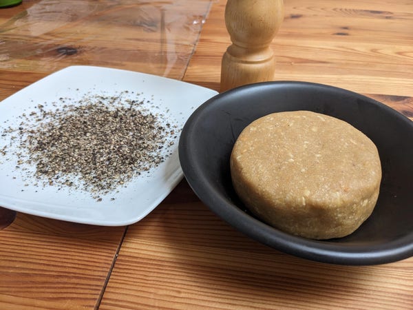 Shaped wheel of cashew cheese, next to a plate of ground pepper.