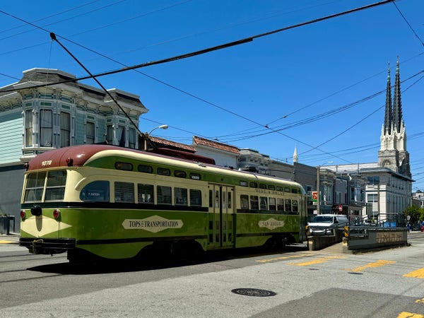 An old MUNI rail car on Church Street. The car is on rails and under an electric wire. It looks old, but well maintained and has a green and yellow color scheme. 