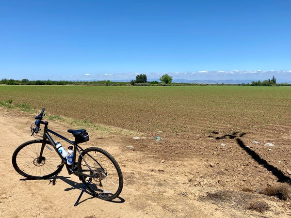 A bicycle stands on a dirt path next to a cultivated field under a clear blue sky.