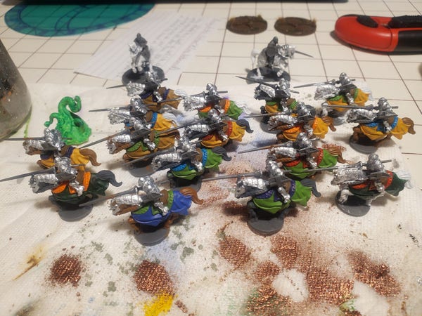 A bunch of mounted knight miniatures with lances, arranged like they're in a charge. The horses are white, brown, and black. Their saddle blankets are a variety of colors and their armor is shiny. They're standing on a paint-streaked paper towel