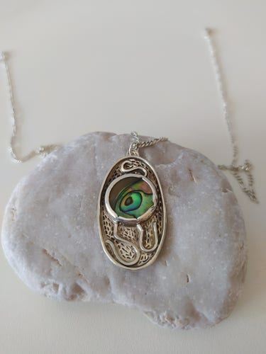 a pendant placed on a pebble. it's oval shaped with a green round gemstone and it has oxidized patterns