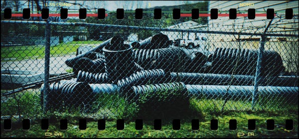 huge sections of plastic pipe (ridged) lying in the grass beyond a barbed wire fence – buildings
