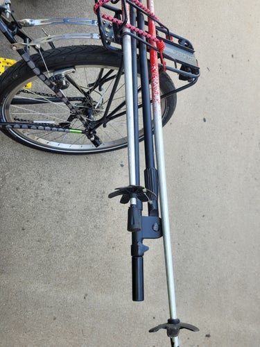 Two ski poles and a microphone rack strapped on a mountain bike, with driveway in background.
