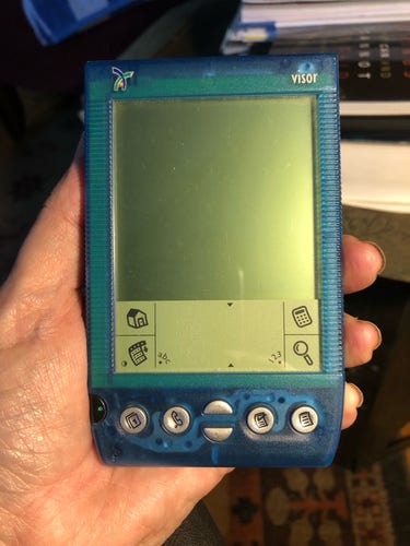 A closeup of an old PDA called the Handspring Visor. It’s translucent blue with an LCD display.