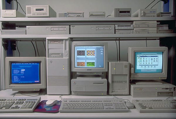 The image shows  photo of a vintage computer setup or lab from the 90s. The monitors are all different sizes and shapes. 
