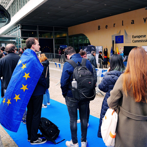 people waiting at the door to enter using an EU flag as a cape