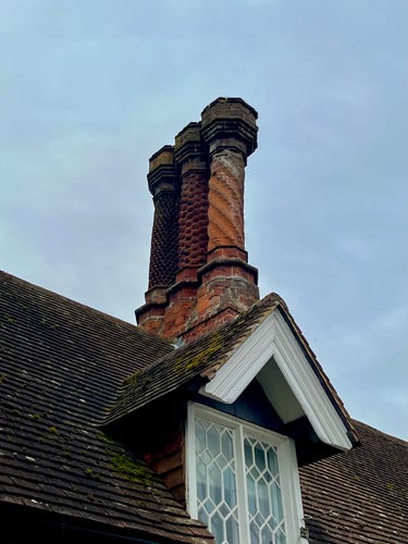 A fancy chimney atop a cottage. There are three stacks, all made in different patterns. They are alarming bendy, but still seem to be in good nick. 