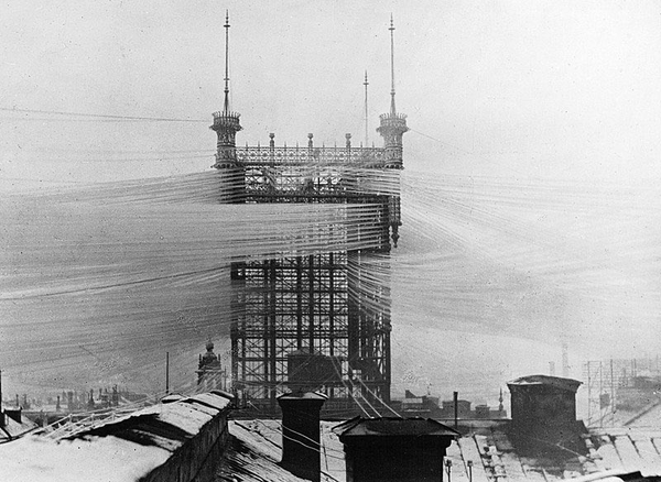 a black and white photo of a telephone tower with millions of wires running to it