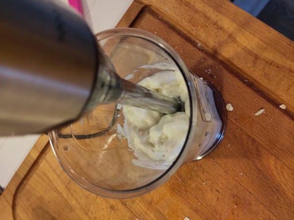 Photo of a hand-held blender blending a white substance in a plastic container.