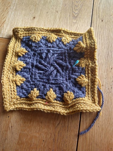 Grey crochet square with yellow border, cross over design with shell edge 