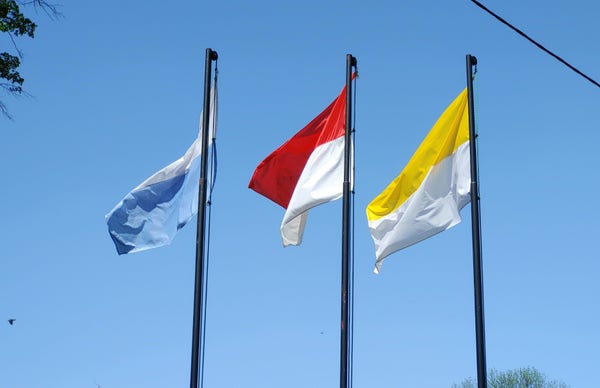Trzy maszty flagowe, dwie flagi kościelne, pośrodku państwowa - do góry nogami.