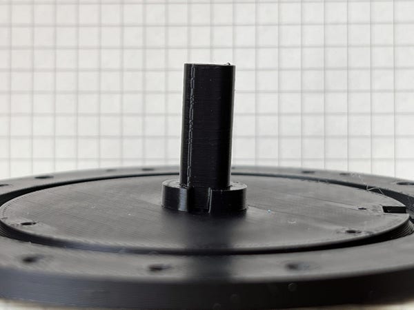 A 3D printed component consisting of a flat disk with a pillar sticking up from it. The pillar looks as though it should be perpendicular to the plate (as it should), but it very visibly isn't.