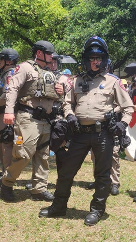 Rather iconic photo of Texas DPS troopers enforcing arrests of Austin protesters. Crop from photo by Kit, linked in post. Both here are in tan uniforms kitted out with all manner of protective gear, helmets, sunglasses and weapons. Both fairly overweight and trying to look menacing. 