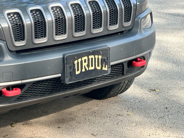 A Purdue license plate cover that has flaked off to say Urdu