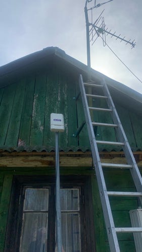 Terminal ODU zamocowany na maszcie, oparty o ścianę. Obok drabiny a na dachu maszt elektryczny i antena tv