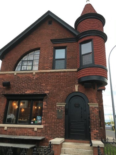 Brick house with mixture of architectural elements including a jutting second story turret, an arched entryway, and  quarter-wheel window