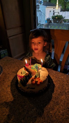 4 year old sitting behind a cake with lit candles in an Anna (from Frozen) dress