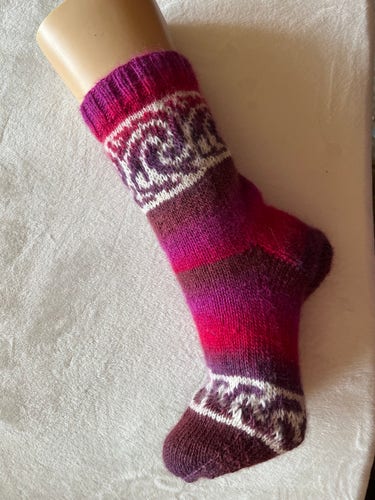 Eine farbenfrohe gestrickte Socke mit lila und rosa Streifen und einem gemusterten Design, das auf einem Mannequin-Fuß dargestellt wird.