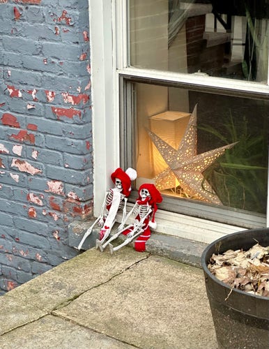 Brooklyn apartment window. Two mini skeletons are placed outside it, wearing red and white knit hats and scarves.