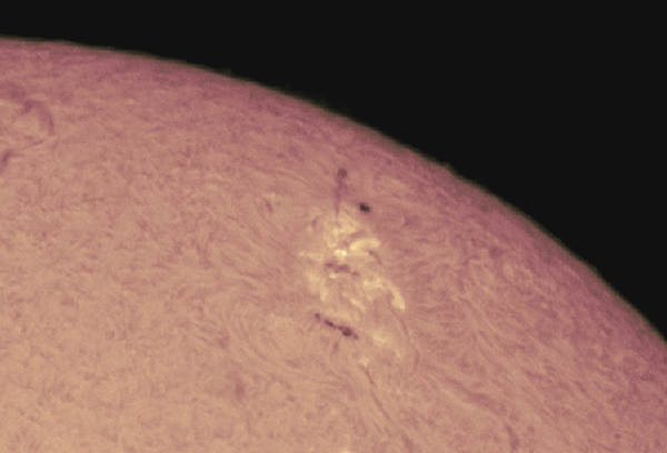 Image of the sun's surface, with a sunspot in view. There's a long dark smudge radiating upward from the sunspot.
