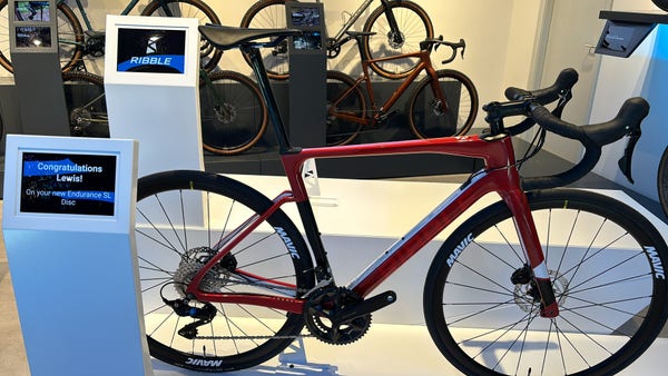 A red Ribble road bike on a showroom stand. The sign says “Congratulations Lewis! On your Endurance SL Disc”