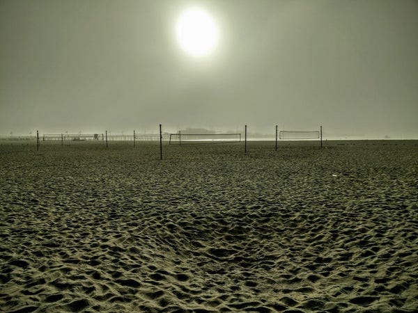 Desolate beach, a blurry sun and abandoned tennis nets. A distant pier behind the nets.