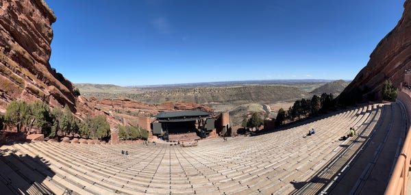 Image from the top of the Red Rocks Amphitheater, its sunny and just a few people are sitting on the steps.