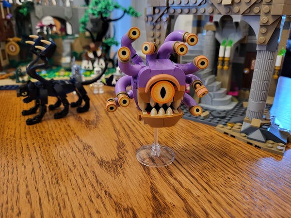 The completed bag 18 of the Lego Dungeons & Dragons set, which consists of a Beholder figure. The center is more or less round, with a huge orange eye above a toothy maw. Around the outside are ten small tentacles, each terminating in a smaller eye. About half of the eyes face forward, and the rest point in random directions. The figure rests on a transparent stick, to represent the way Beholders float in mid-air.
