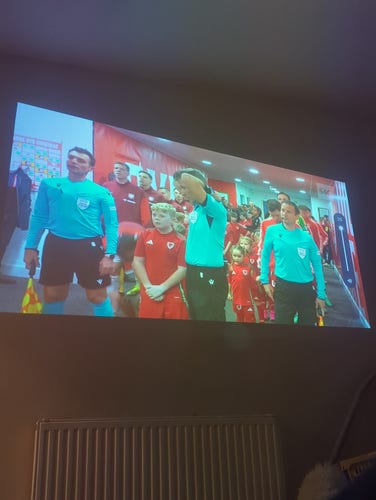 Picture of a projector showing some football players with mascots in the tunnel