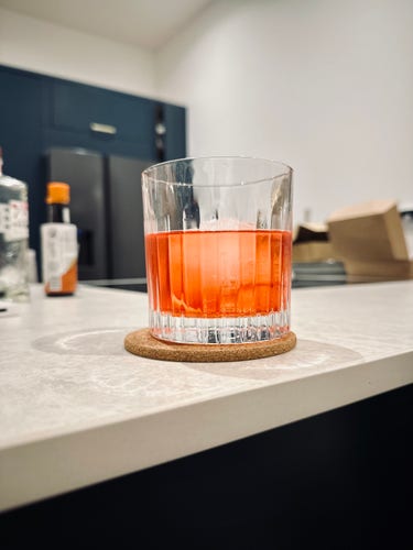 A rocks glass on a kitchen worktop, filled with a bright red drink and a big sphere of chonky ice