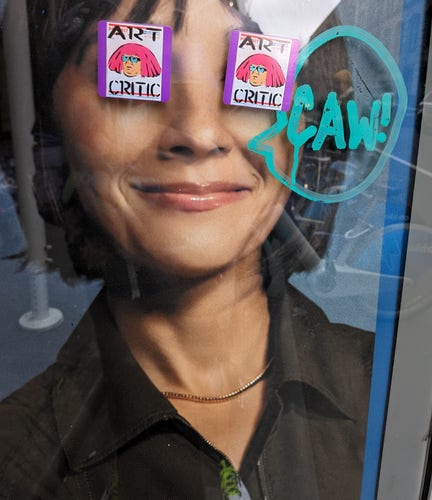 Two stickers of Danny Devito as an art critic cover the eyes of Rashida Jones on a citybike poster ad. Someone drew a word bubble that has her saying "caw". I won't know what that means