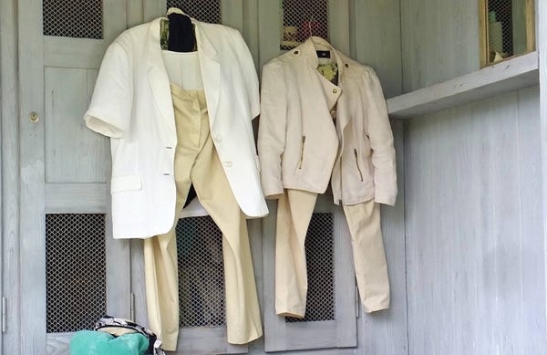 Auf zwei Bügel hängende Kleidungstücke an Garderobenkästen: Jacken, Hosen, Shirts. 