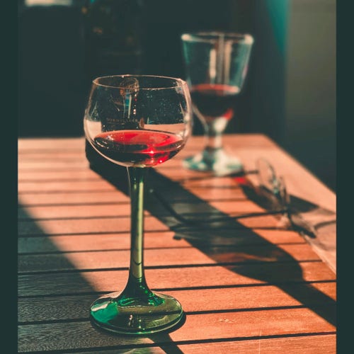 A glass of red wine is standing on a brown table. In the background you see glasses on the right hand side and another glass of red wine.