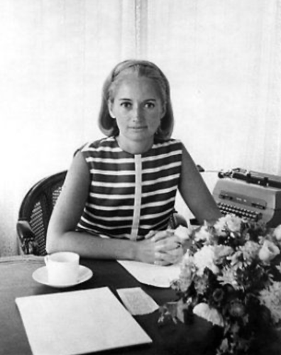 Mary Wells Lawrence seen at her office desk surrounded by flowers, typewriter, papers.