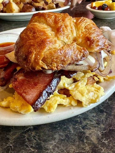 A croissant sandwich with bacon, eggs, and onions on a plate, suggesting a breakfast setting.