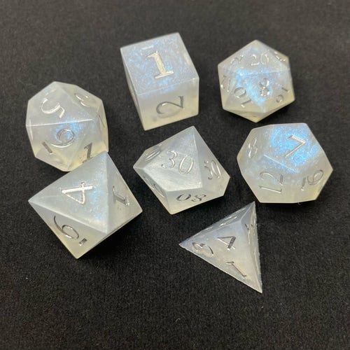 A set of 7 RPG dice in various geometric polygons, the resin is translucent but slightly cloudy from the powders, with clouds and swirls of electric blue, and tiny flashes of silver glitter. The dice numbers are inked in Liquid Chrome paint, which also worked better than I expected