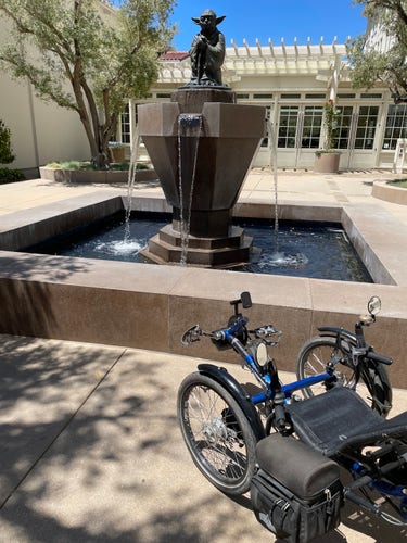 A statue of Yoda from Star Wars atop a concrete fountain in a courtyard. In the foreground is a recumbent trike. 