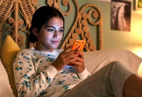 Isabela Merced reclines on her bed. She's looking at her phone. 